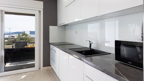 A modern kitchen with white cabinets, a black countertop, and a view of the outdoors through a sliding door. - Holiday Home Miriam Kastela With a Private Pool (Kastela)