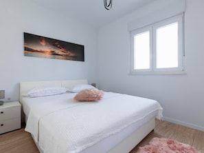Een slaapkamer met een bed, nachtkastje, raam en een schilderij aan de muur.