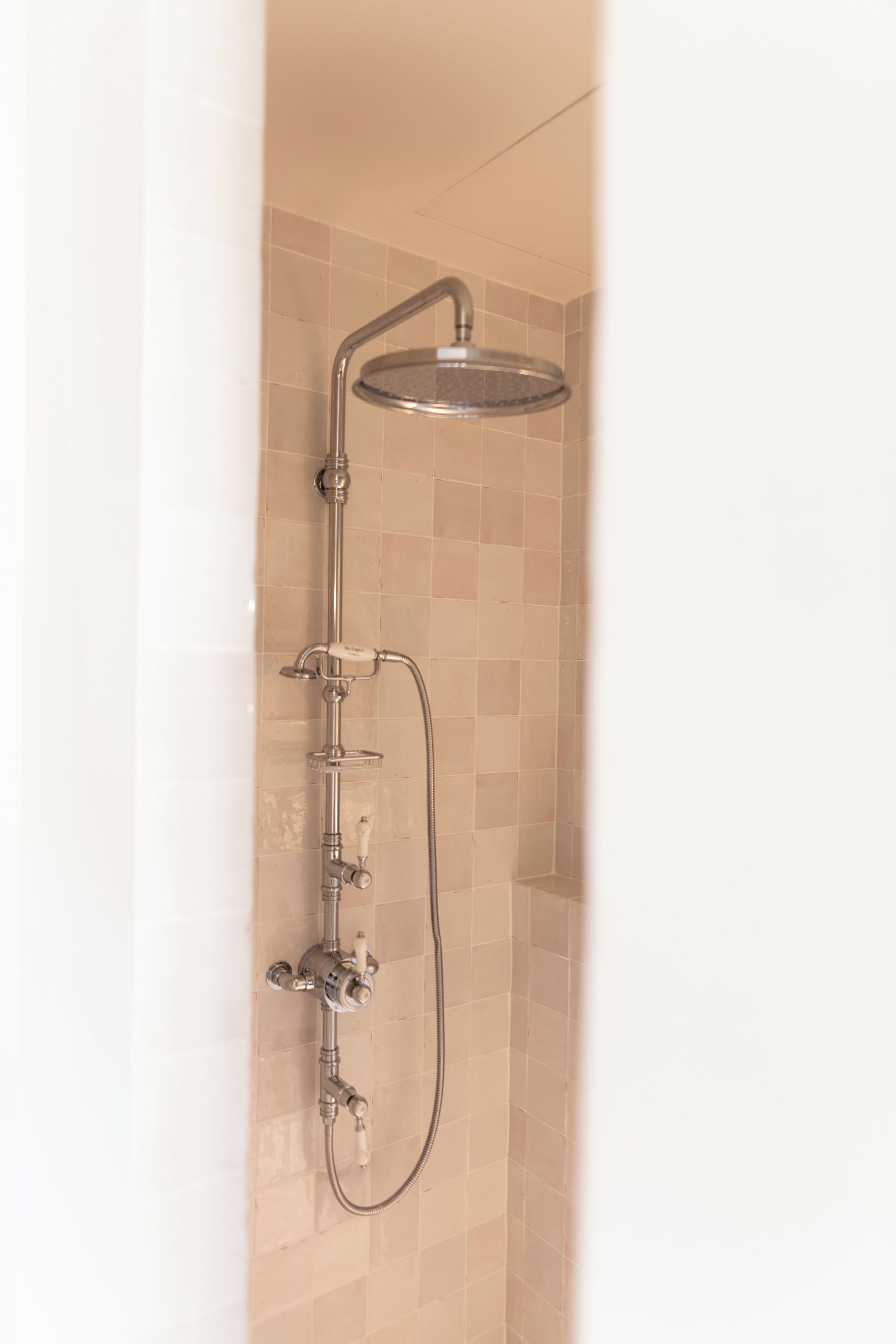 A shower with a handheld showerhead and a fixed overhead showerhead, mounted on a tiled wall.