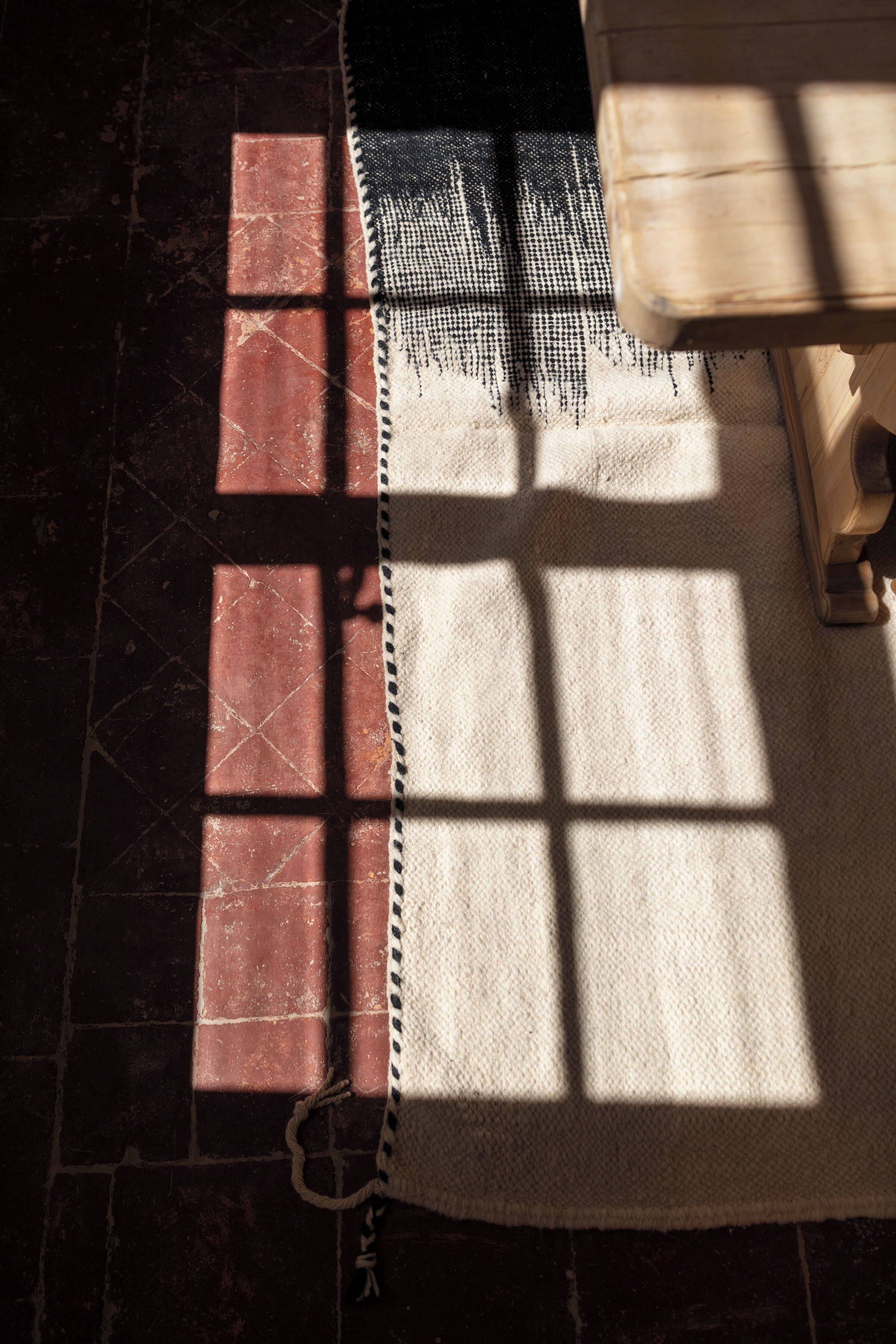Una habitación con alfombra estampada, un banco de madera y suelo de baldosas.