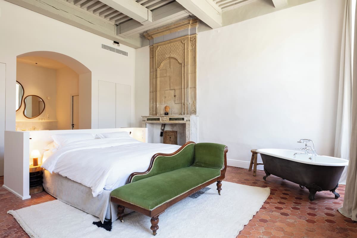 Un dormitorio con una cama, un sofá verde, una bañera de patas de león y un espejo en la pared.