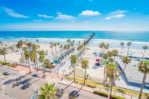 A beachside view with palm trees, a pier, and a parking area.