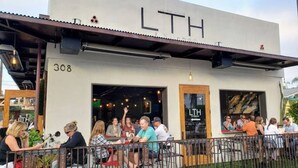 Ein Sitzbereich im Freien eines Restaurants mit einer modernen Fassade und der Beschriftung 'LTH'.