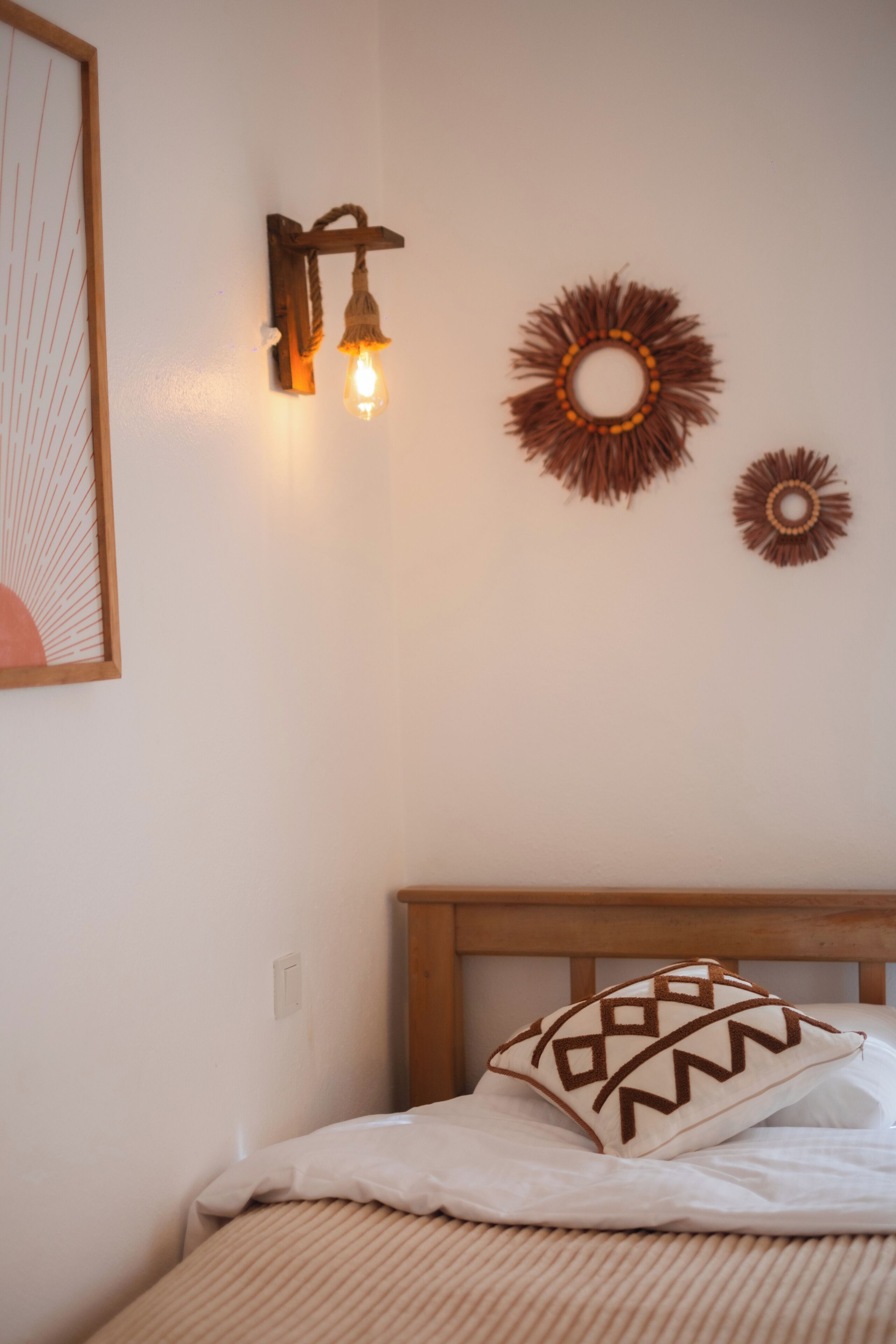 A neatly made bed with a wooden headboard, a wall-mounted light fixture, and two wall decorations.