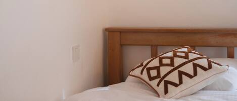 A neatly made bed with a wooden headboard, a wall-mounted light fixture, and two wall decorations.