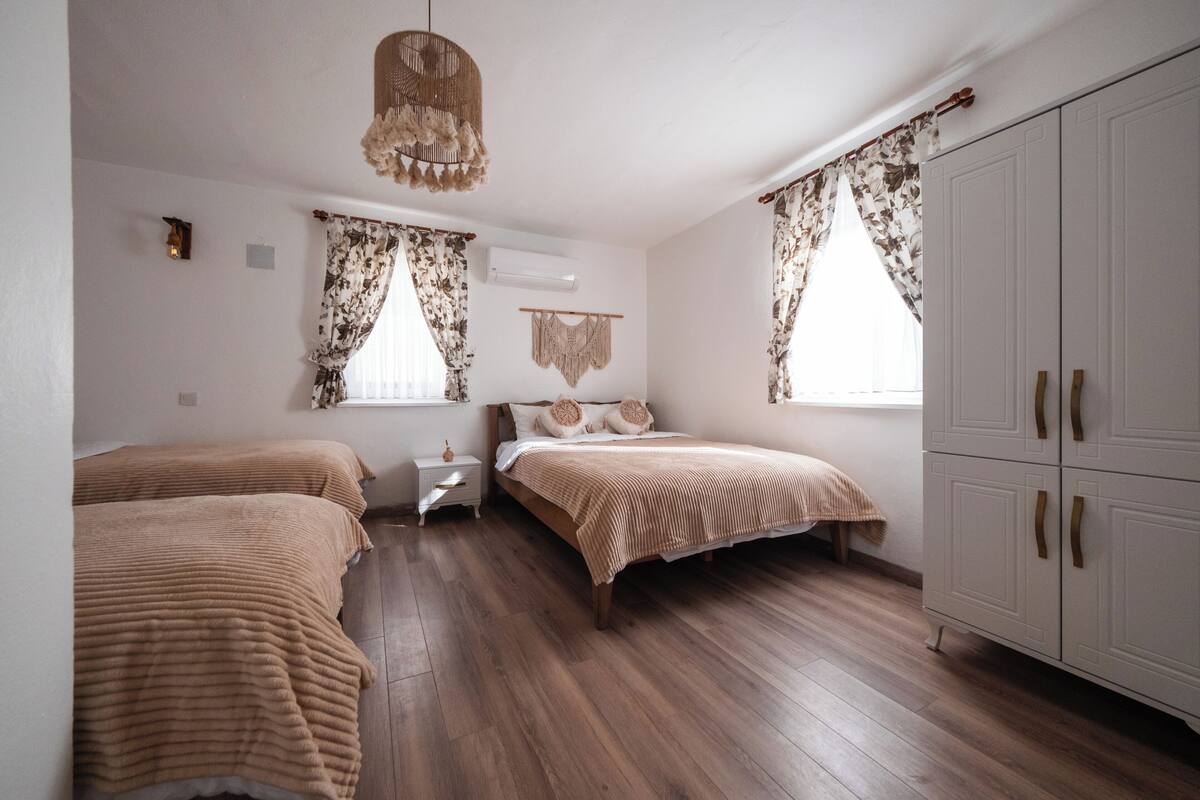 A bedroom with two beds, wooden flooring, a wardrobe, and a hanging light fixture.