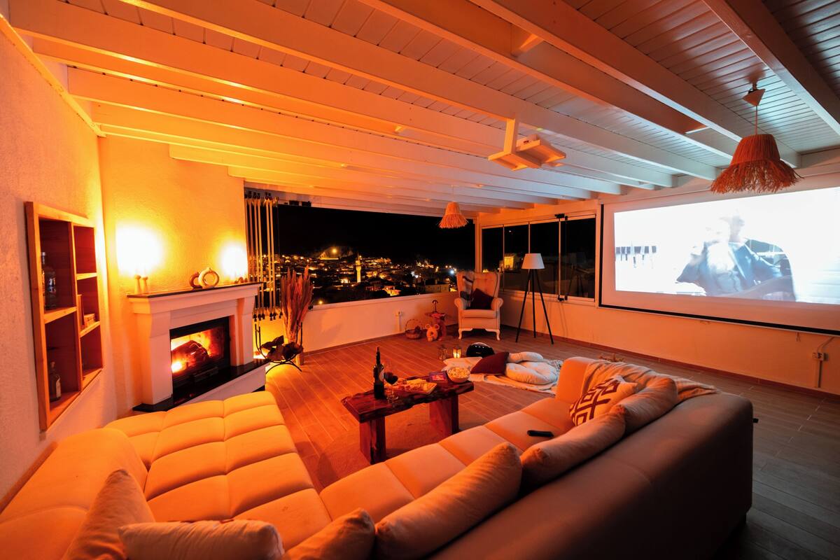 A cozy living room with a fireplace, comfortable seating, and a large screen for viewing.