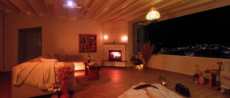 A cozy bedroom with a fireplace, a sofa, and a view of the city at night.