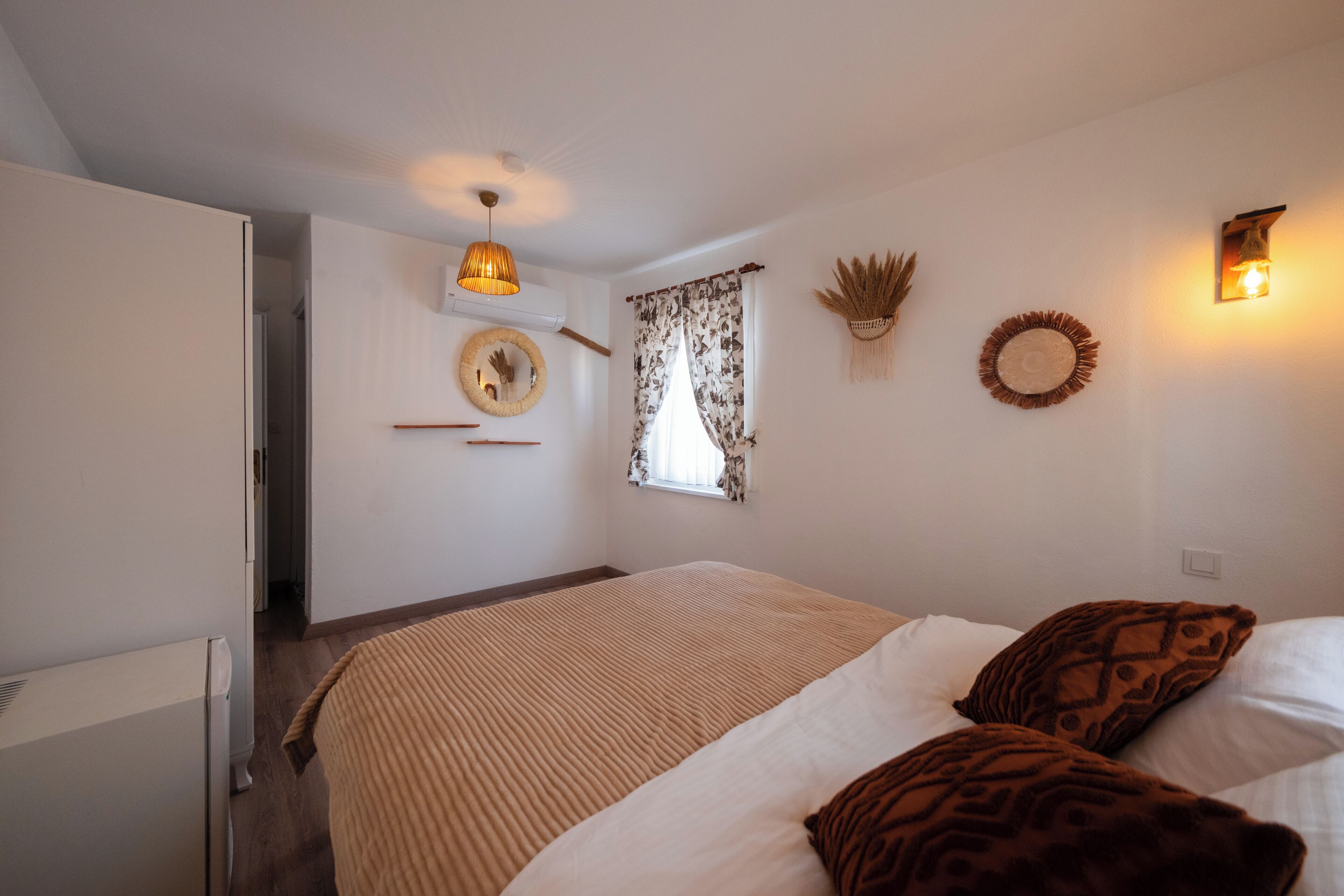 Une chambre à coucher comprenant un lit, un radiateur, une lampe fixée au mur, une fenêtre avec des rideaux et un élément décoratif mural.