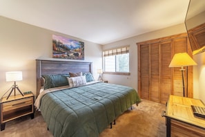 A bedroom with a bed, a nightstand, a lamp, a painting, a window, and a wooden closet.
