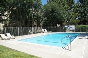 A swimming pool with lounge chairs, a metal fence, and a caution sign. - Large and Comfortable Condo w/ Loft (Mammoth Lakes)