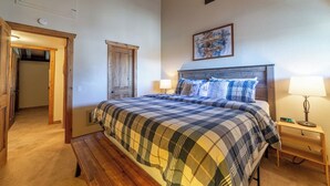 A bedroom with a bed, a bench, a nightstand, a wall clock, a door, and a framed picture. - Large and Comfortable Condo w/ Loft (Mammoth Lakes)