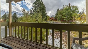 A wooden deck with a view of a mountain range, trees, and a building. - Large and Comfortable Condo w/ Loft (Mammoth Lakes)