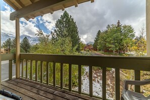 A wooden deck with a view of a mountain range, trees, and a building. - Large and Comfortable Condo w/ Loft (Mammoth Lakes)