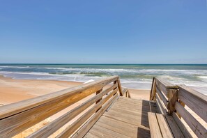 A wooden boardwalk leading to a beach with waves crashing onto the shore. - Oceanfront Ormond Beach Condo: Patio, Pool Access! (Ormond Beach)