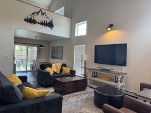 Een woonkamer met een bank, salontafel, poef en een flatscreen televisie aan de muur.