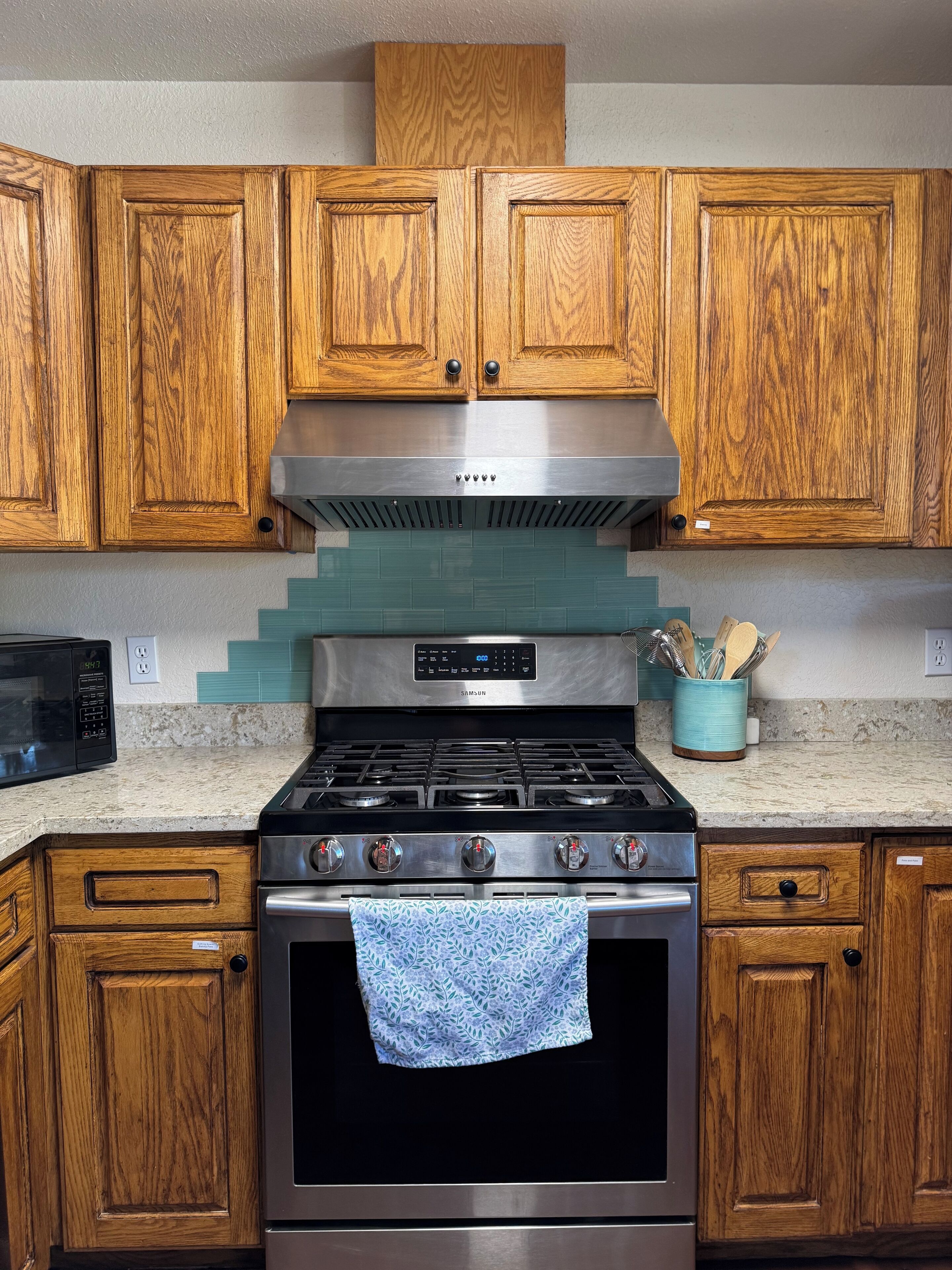 Une cuisine avec des meubles de rangement en bois, une hotte de cuisinière en acier inoxydable, un four à micro-ondes et une cuisinière.