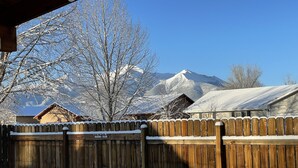 Une clôture en bois recouverte de neige, une maison en bois et une montagne en arrière-plan.