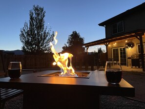 Un patio con una chimenea, mobiliario exterior y un área techada decorada con luces colgantes.