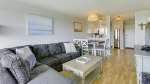 En moderne stue med en grå modulsofa, et træsofabord og et spiseområde med hvide stole og et bord.