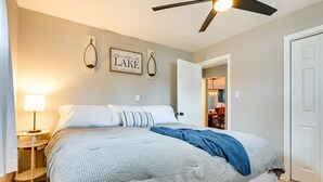 A bedroom with a bed, bedside tables, a ceiling fan, and a door leading to another room. - Sand Lakefront Retreat | Private Dock & Fire Pit (Harrison)