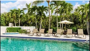 Un espace aménagé au bord de la piscine, avec des chaises longues et des parasols, entouré de palmiers.