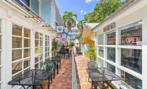 A narrow outdoor corridor with tables and chairs, surrounded by buildings with large windows and a 'OPEN' sign.