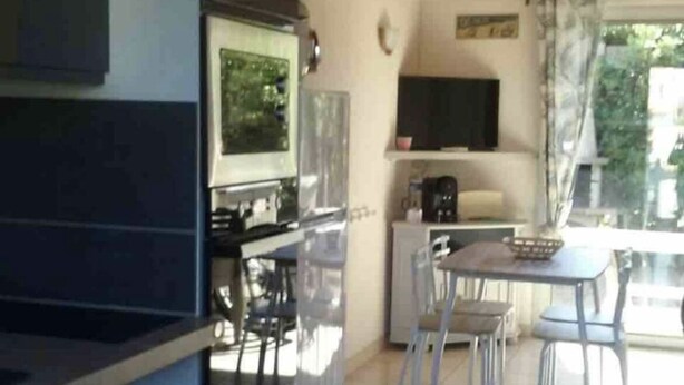 A compact kitchen with a washing machine, a dining area with chairs, and a TV on the wall. - House la franqui (Occitanie)