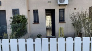 A two-story building with a white picket fence, a front door, and a small garden area. - House la franqui (Occitanie)
