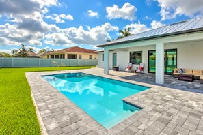 Piscina com deck pavimentado, área de varanda coberta com mobiliário externo e vista para casas vizinhas.