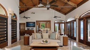 A spacious living area with a high ceiling, wooden beams, and a large central coffee table.