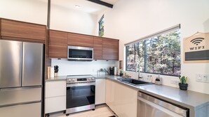 Uma cozinha moderna com eletrodomésticos de aço inoxidável, armários de madeira e uma janela ampla com vista para árvores.