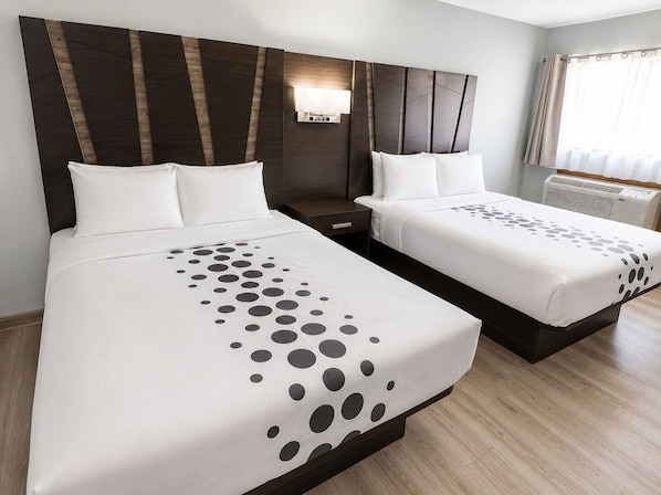 Habitación de hotel con dos camas, una mesita de noche, una lámpara de pared y un ventanal con cortinas.