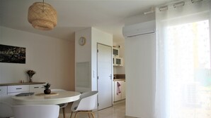 A modern kitchen with white cabinets, a dining table with chairs, a hanging light fixture, and a large window with sheer curtains. - Serignan-Canal du midi. Spacious apartment in luxury apartment complex. Full A/C (Sérignan)