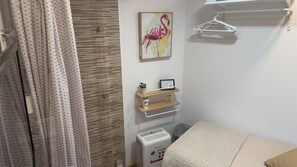 A bedroom with a bed, a heater, a wall-mounted shelf with a picture, and a hanging clothes rack.