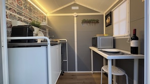 A compact kitchen with a microwave, a small fridge, a sink, and a wine bottle on a shelf.