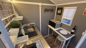 A compact kitchen with a sink, microwave, and a small dining table with a wine bottle. - Independent Studio Room, with equipped mini kitchen and private patio. (Olhão)