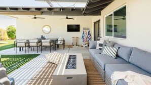 A covered patio area with a sofa, a dining table, and chairs. There are flags on the wall and a television mounted above the table. - Family-Friendly Retreat with Heated Pool (Scottsdale)