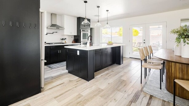 A modern kitchen with a central island, black cabinets, and a dining area with wooden chairs and a table. - Family-Friendly Retreat with Heated Pool (Scottsdale)