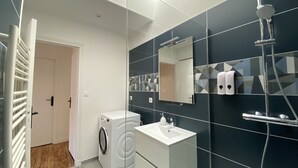Un baño moderno con lavadora, lavamanos, espejo y ducha.