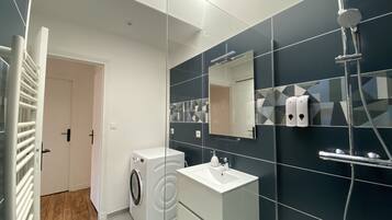 Une salle de bain moderne équipée d’un lave-linge, d’un évier, d’un miroir et d’une douche.