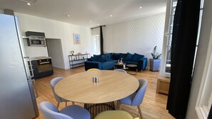 Cocina moderna con refrigerador, microondas y estufa. Hay un comedor con una mesa redonda y sillas. Un sofá azul y una mesita auxiliar se encuentran en la sala.