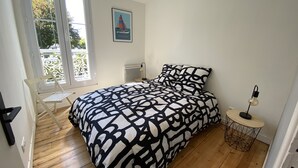 Un dormitorio con cama, una silla, una mesita y un radiador.