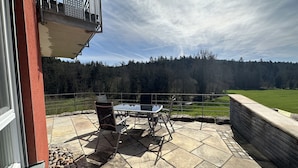 Un patio con una mesa y sillas, piso de piedra y vista a un área boscosa.