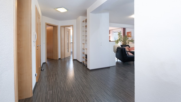 Un pasillo moderno con puertas de madera, una estantería empotrada y una zona de estar con sofá y mesa de centro.