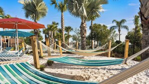 A hammock area with striped fabric and wooden posts, surrounded by palm trees and a clear sky.