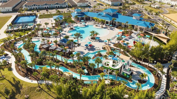 An aerial view of a resort with a large central pool, multiple smaller pools, and a variety of amenities including a water slide and lounge areas.