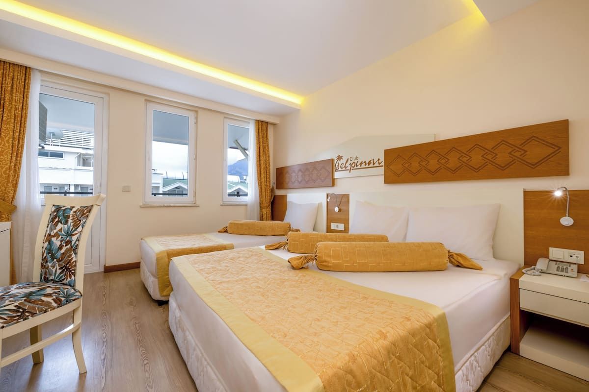Une chambre d’hôtel avec deux lits, une chaise, une table de chevet et une fenêtre avec des rideaux.