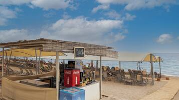 A beachside bar with a Coca-Cola cooler, lounge chairs, and umbrellas.