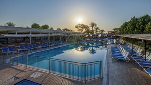 Piscina com o sol refletindo na água, rodeada por espreguiçadeiras e guarda-sóis.